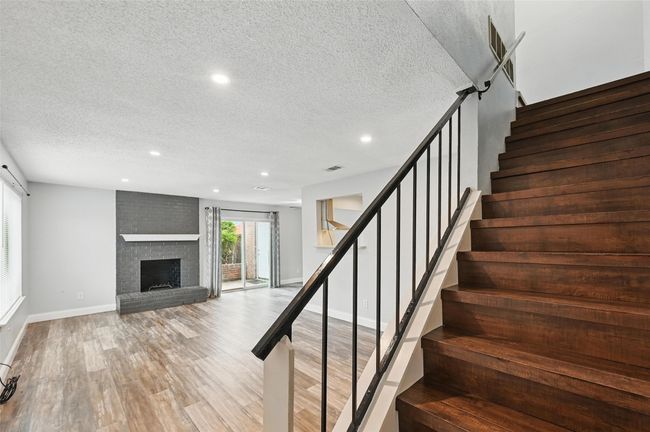 Staircase featuring a textured ceiling, wood finished floors, recessed lighting, and a brick fireplace | Image 11