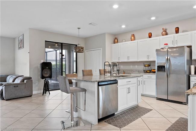 Kitchen with light tile patterned flooring, stainless steel appliances, a center island with sink, white cabinetry, and a sink | Image 10