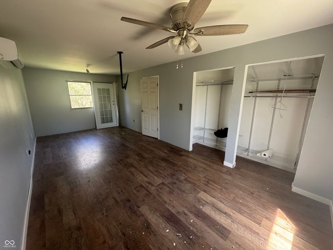 unfurnished bedroom featuring baseboards, a wall mounted AC, dark wood-type flooring, two closets, and a ceiling fan | Image 12