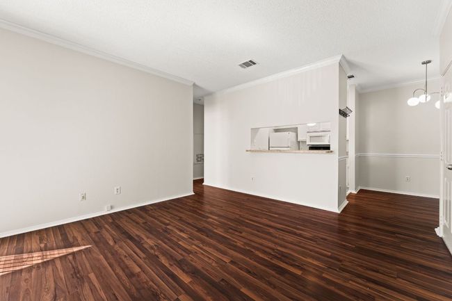 Unfurnished living room with wood finished floors, visible vents, baseboards, crown molding, and a notable chandelier | Image 5