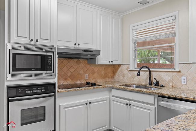 Kitchen with appliances with stainless steel finishes, a sink, under cabinet range hood, white cabinets, and decorative backsplash | Image 6