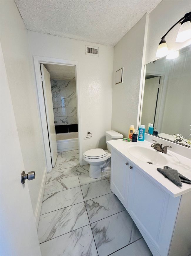 Bathroom with marble finish flooring, toilet, vanity, a textured ceiling, and baseboards | Image 13