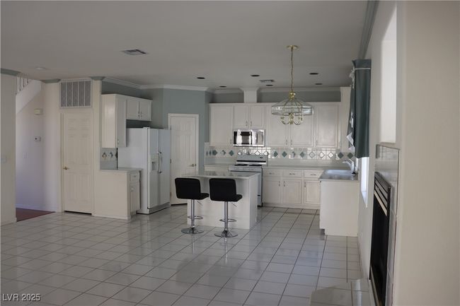Kitchen featuring white appliances, tasteful backsplash, a center island, a kitchen bar, and white cabinets | Image 31