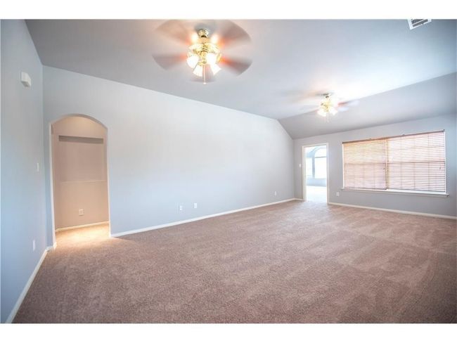 Carpeted empty room featuring a ceiling fan, arched walkways, vaulted ceiling, and baseboards | Image 12