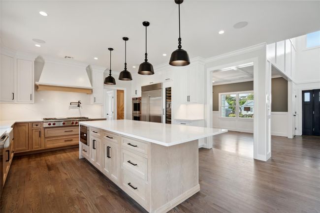 Kitchen with wall chimney range hood, stainless steel appliances, dark wood-style flooring, light countertops, and a kitchen island | Image 7