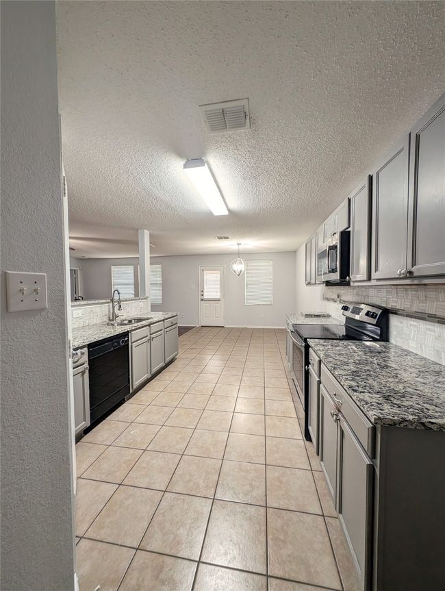 Kitchen featuring appliances with stainless steel finishes, decorative backsplash, a textured ceiling, a sink, and light tile patterned flooring | Image 5
