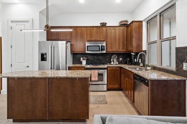 Kitchen with stainless steel appliances, a sink, light wood-type flooring, backsplash, and light stone counters | Image 8