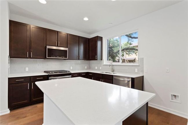 Kitchen with stainless steel appliances, light wood-style flooring, decorative backsplash, light countertops, and recessed lighting | Image 10