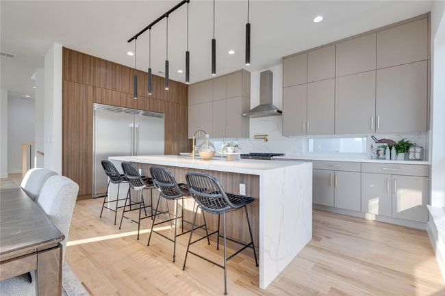 Kitchen featuring hanging light fixtures, a kitchen island with sink, stainless steel built in fridge, wall chimney range hood, and light hardwood / wood-style flooring | Image 13