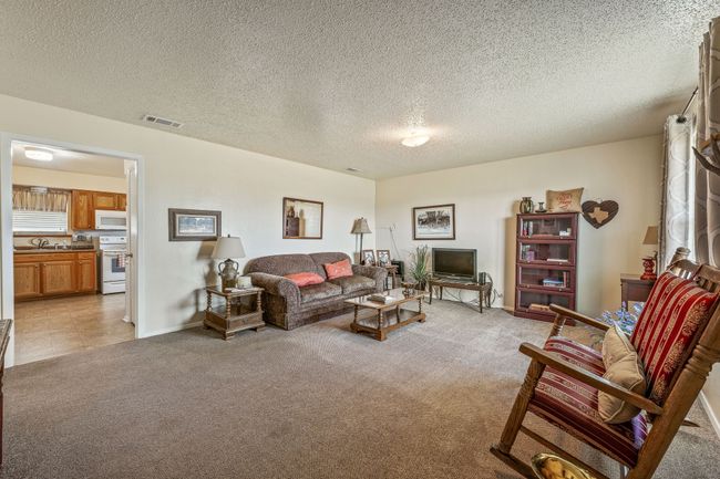 Living area featuring a textured ceiling, light colored carpet, baseboards, and visible vents | Image 8