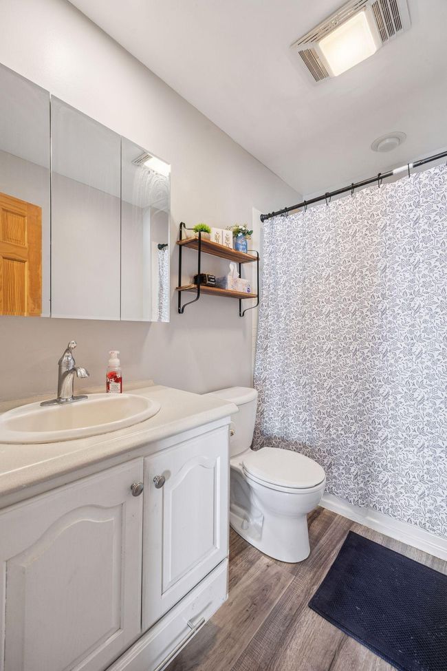 The main floor bathroom is both stylish and functional, featuring a vanity sink with storage, a mirrored cabinet, durable LVP flooring, and a full tub and shower combination for convenience and comfort. | Image 11
