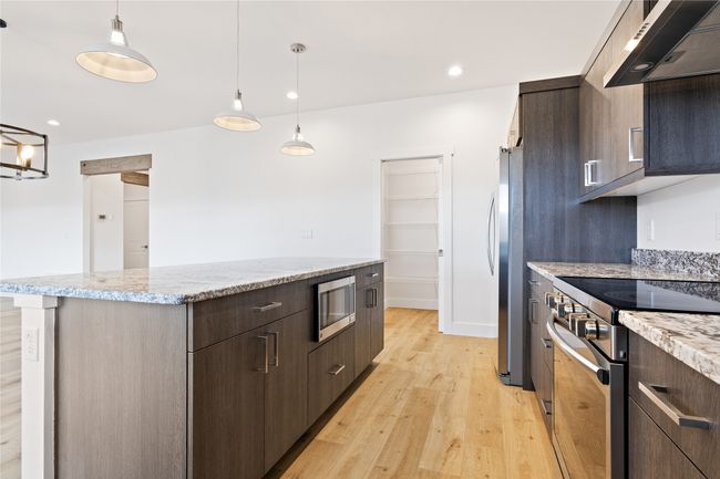 Kitchen featuring stainless steel appliances, ventilation hood, a center island, dark brown cabinets, and light wood-style flooring | Image 12