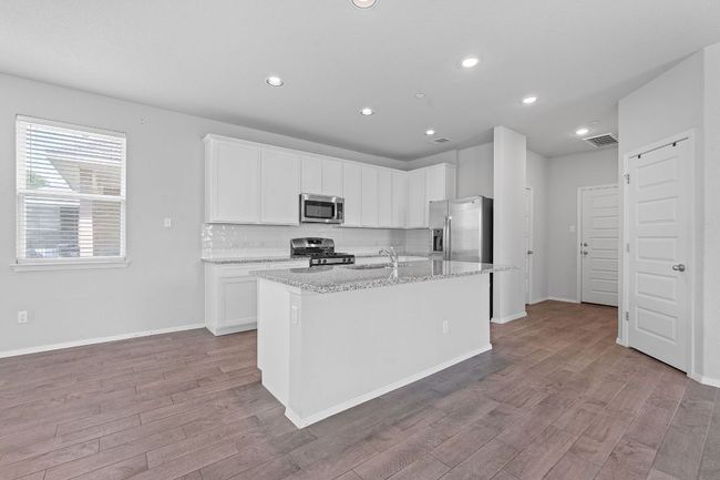 Kitchen featuring stainless steel appliances, wood finished floors, light stone counters, white cabinetry, and recessed lighting | Image 9