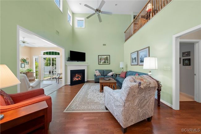 Living area featuring ceiling fan, a towering ceiling, a glass covered fireplace, wood finished floors, and plenty of natural light | Image 5