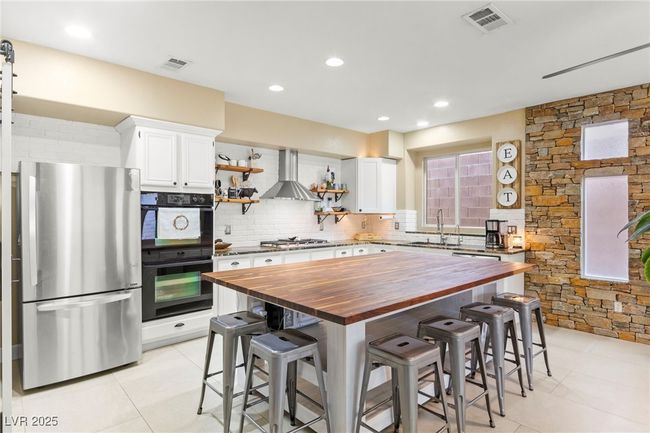 Kitchen with butcher block countertops, appliances with stainless steel finishes, wall chimney range hood, open shelves, and tasteful backsplash | Image 11