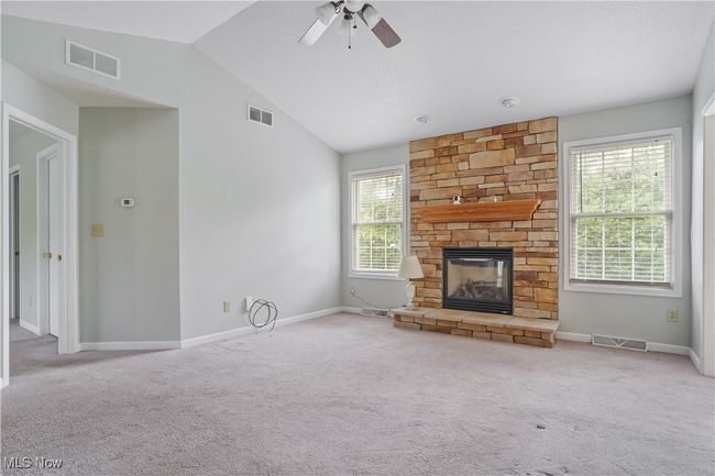 Unfurnished living room featuring vaulted ceiling, carpet floors, a ceiling fan, baseboards, and a stone fireplace | Image 14