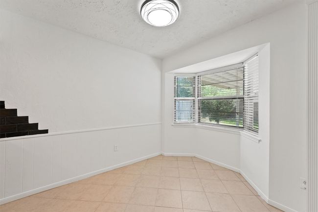 Bright and airy nook with large bay window, neutral tile flooring, and modern ceiling light. Ideal for a cozy dining or sitting area with a view of the backyard. | Image 11