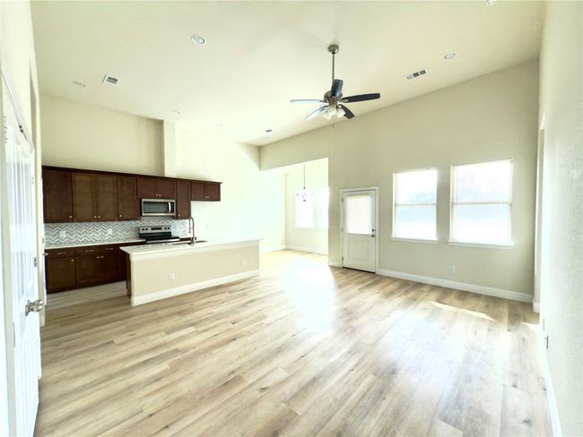 Kitchen featuring appliances with stainless steel finishes, open floor plan, a ceiling fan, light wood-style flooring, and a center island with sink | Image 16