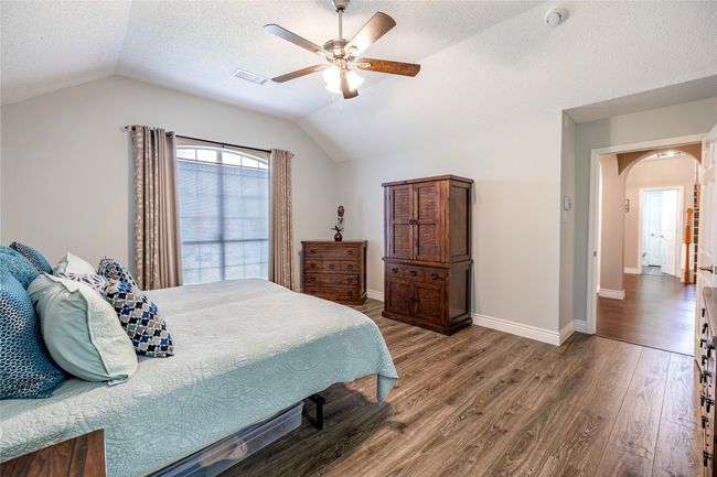 Bedroom featuring vaulted ceiling, arched walkways, wood finished floors, a textured ceiling, and baseboards | Image 21