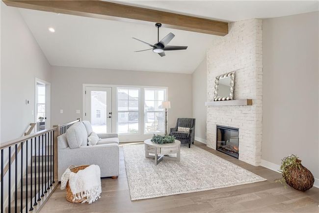 Living room with wood finished floors, beamed ceiling, a ceiling fan, and a stone fireplace | Image 7