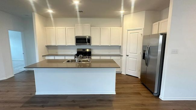 Kitchen featuring appliances with stainless steel finishes, a center island with sink, white cabinetry, and dark wood-style flooring | Image 5