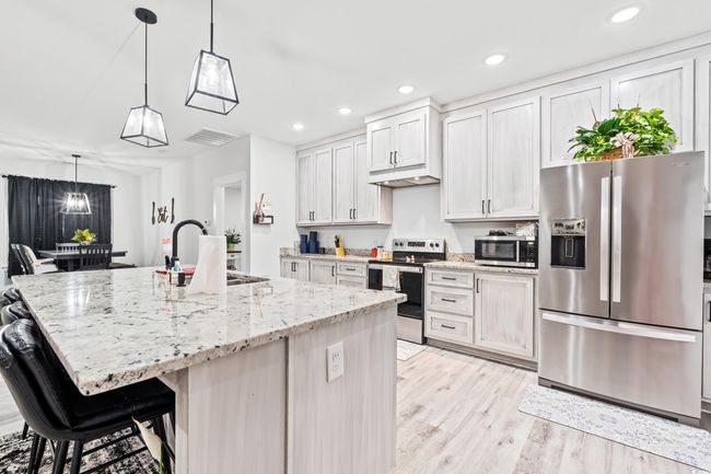 Kitchen with appliances with stainless steel finishes, light wood finished floors, an island with sink, light stone counters, and recessed lighting | Image 8