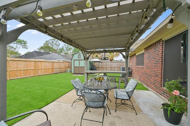 Enjoy outdoor living under the pergola-covered patio, complete with string lights, bar seating, and a dining space perfect for entertaining. The fully fenced backyard offers lush green lawn space and a storage shed for added convenience. | Image 22