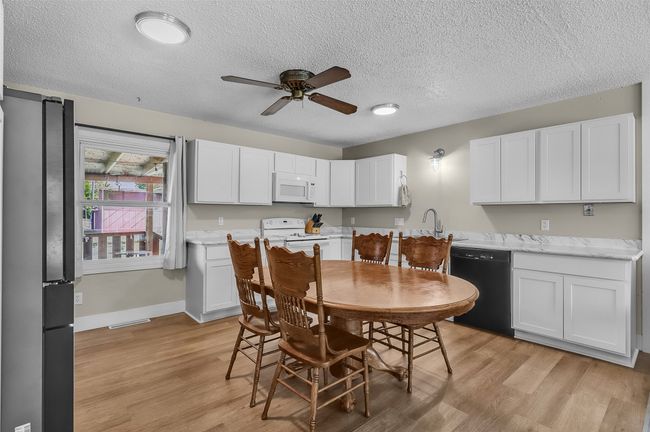 Kitchen with white appliances, a ceiling fan, a textured ceiling, white cabinets, and light wood-type flooring | Image 10