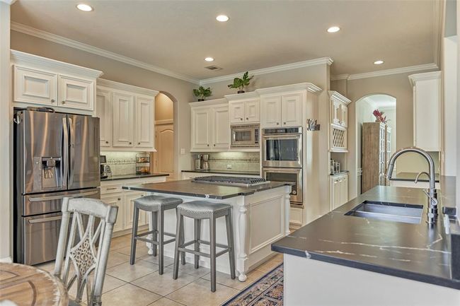 Sleek open-concept kitchen featuring updated stainless steel appliances, a functional gas stove on the island, and stunning leathered quartzite countertops. | Image 10