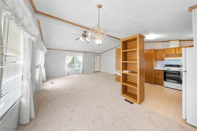 Unfurnished living room featuring light carpet, ceiling fan, lofted ceiling, a chandelier, and crown molding | Image 6