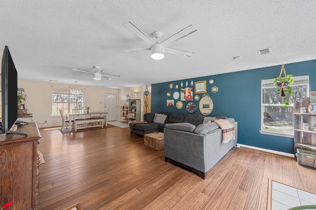 Living room featuring wood finished floors, a textured ceiling, ceiling fan, baseboards, and visible vents | Image 7