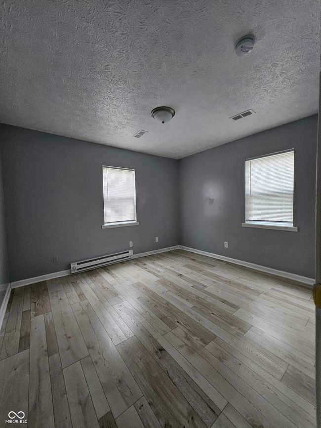 empty room with a baseboard radiator, hardwood / wood-style flooring, a textured ceiling, and baseboards | Image 9