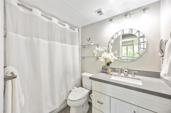 This newly updated bathroom is modern and bright, featuring a sleek vanity, gray countertop, and elegant lighting. | Image 17