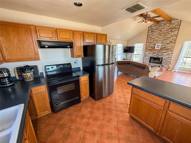 Kitchen featuring range hood, freestanding refrigerator, dark countertops, visible vents, and black electric range | Image 12