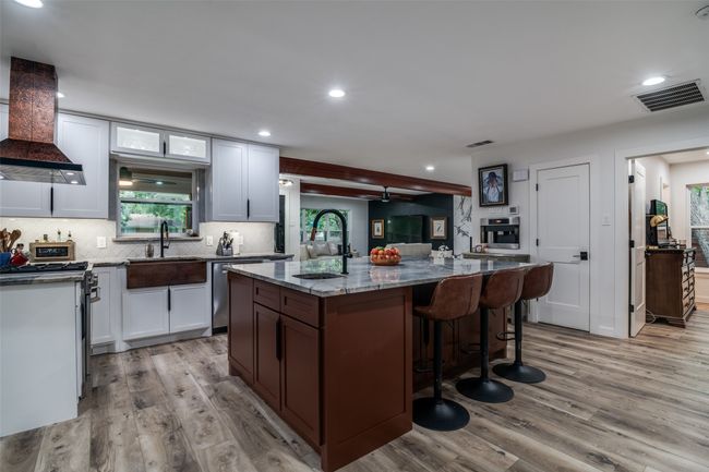 Kitchen featuring wall chimney exhaust hood, appliances with stainless steel finishes, light wood-type flooring, dark stone counters, and backsplash | Image 12
