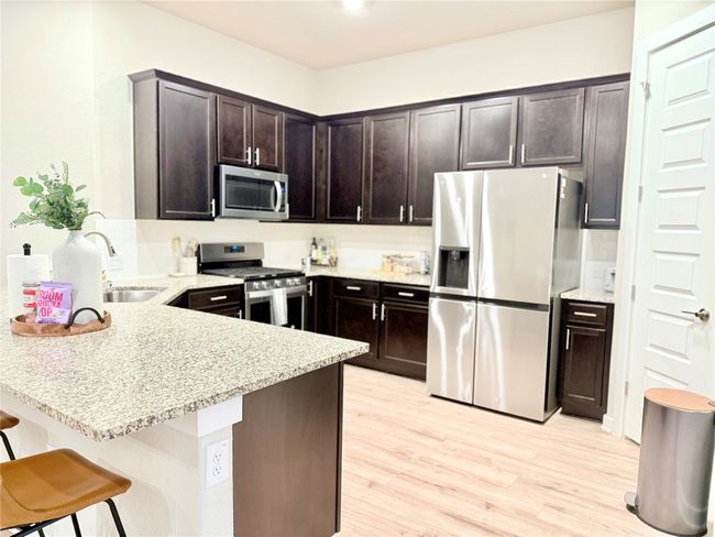 Kitchen featuring a peninsula, dark brown cabinets, a sink, stainless steel appliances, and light wood-type flooring | Image 5