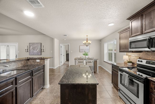 Kitchen with appliances with stainless steel finishes, a chandelier, backsplash, light tile patterned flooring, and dark brown cabinetry | Image 13