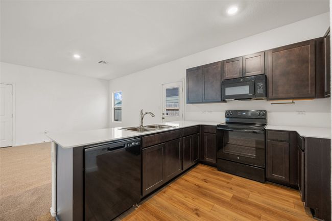 Kitchen with black appliances, a peninsula, dark brown cabinetry, light countertops, and recessed lighting | Image 20