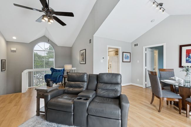 Living room with vaulted ceiling, light wood finished floors, rail lighting, ceiling fan, and baseboards | Image 15