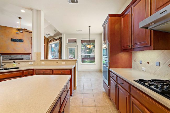 Kitchen featuring a sink, light tile patterned floors, stainless steel appliances, light countertops, and under cabinet range hood | Image 13