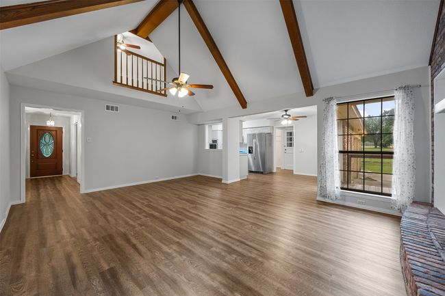 Unfurnished living room featuring ceiling fan, high vaulted ceiling, wood finished floors, beam ceiling, and baseboards | Image 10