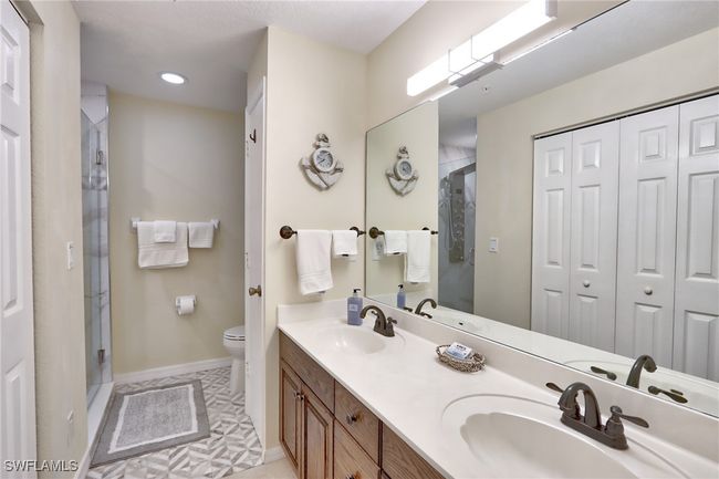 Bathroom featuring dual sinks, tile flooring, vanity with extensive cabinet space, a shower with door, and toilet | Image 14