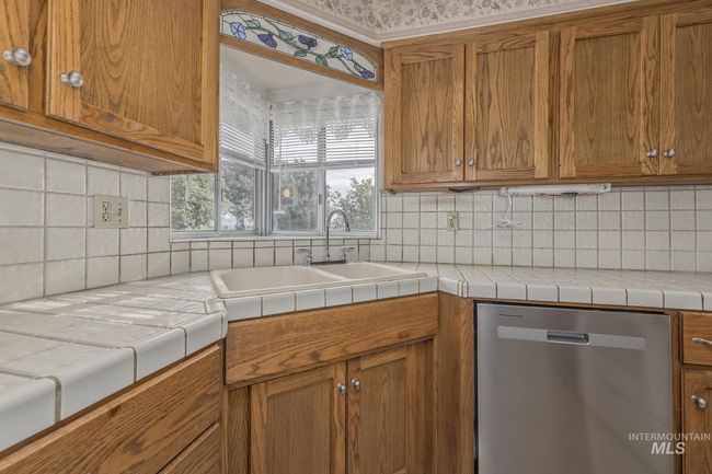 Kitchen featuring brand new stainless steel dishwasher, brown cabinetry, and tile backsplash | Image 11