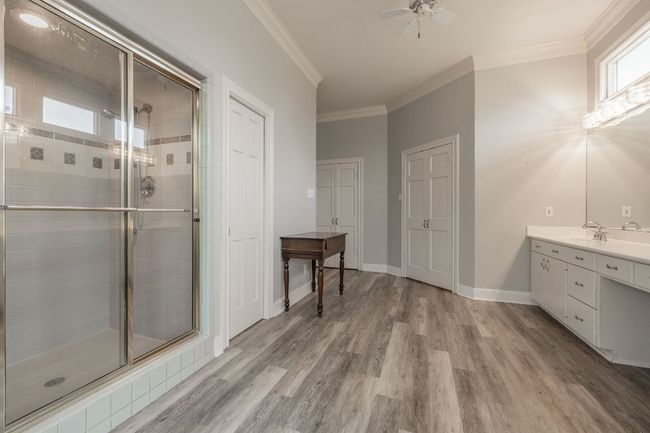 Bathroom with a shower, double vanity, wood floors, a ceiling fan, and crown molding | Image 22
