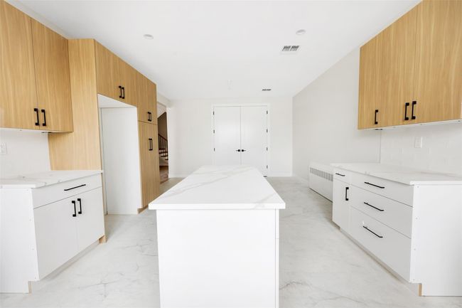 Kitchen with radiator, a center island, white cabinets, and light brown cabinets | Image 22