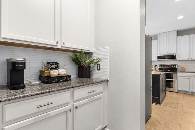 Kitchen featuring stainless steel appliances, tasteful backsplash, light tile patterned floors, white cabinets, and stone counters | Image 12