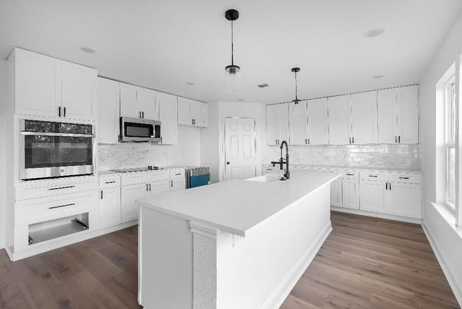 Kitchen featuring white cabinets, backsplash, stainless steel appliances, and dark wood-style flooring | Image 6