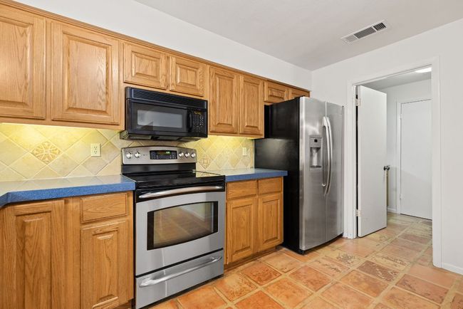 Kitchen featuring stainless steel appliances, tasteful backsplash, dark countertops, and brown cabinetry | Image 10