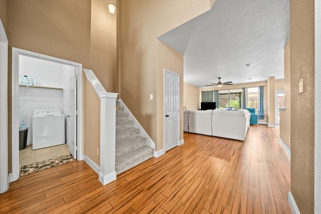 Unfurnished living room with washer / clothes dryer, light wood-style flooring, ceiling fan, stairs, and baseboards | Image 10