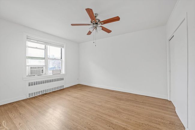Unfurnished room with radiator heating unit, light wood finished floors, a ceiling fan, and cooling unit | Image 6